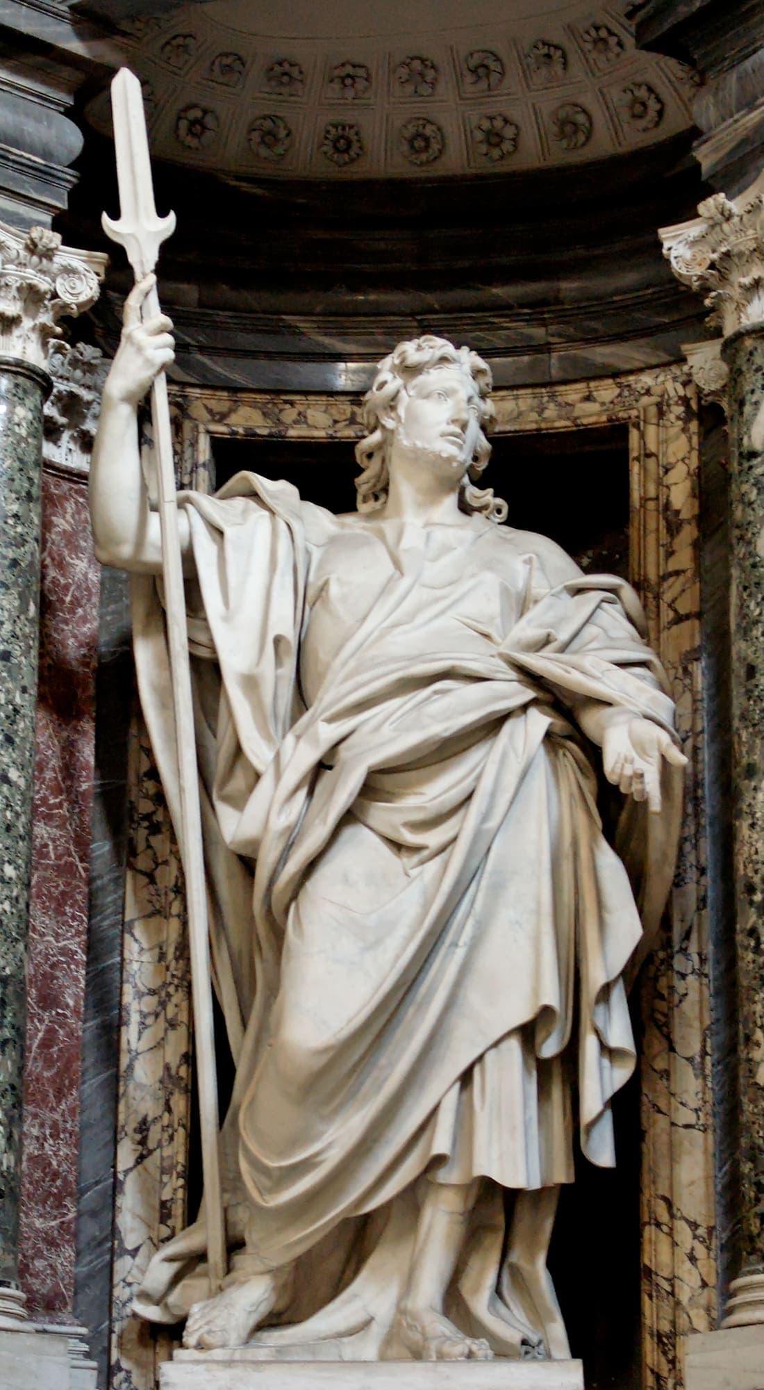 A white marble statue of St. Jude Thaddeus standing in a niche of coloured marble at the Basilica of St. John Lateran in Rome, holding a tall halberd and looking upward